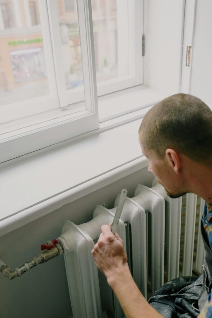 installateur-website-kitzingen Installateur bei der Arbeit, im Hintergrund ein Heizkörper. Symbolisiert Fachkompetenz für Sanitär & Heizung in Kitzingen.